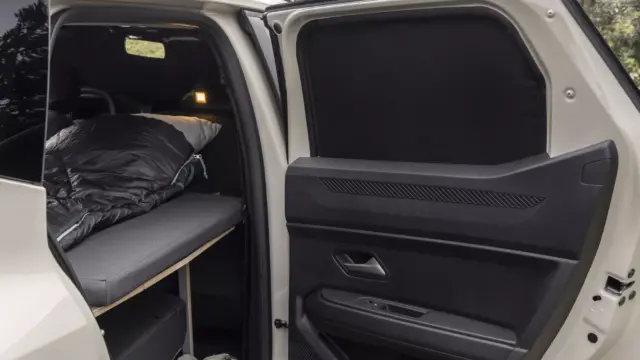 Open SUV rear with a built-in bed: grey cushions, sleeping bag, pillow, and shoes on the floor.