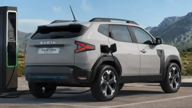 Dacia Duster Electric SUV charging at a station with mountains in the background.