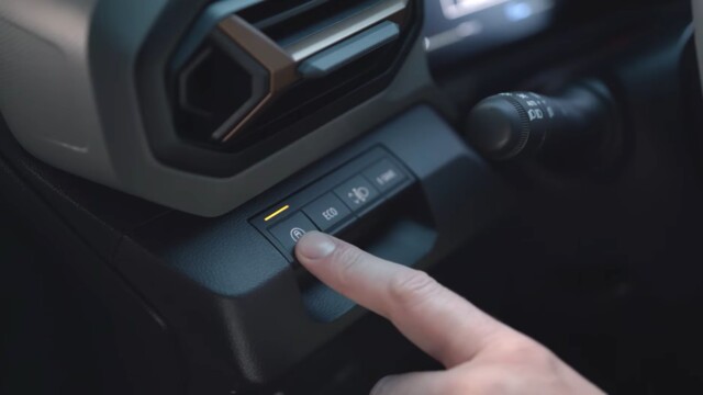 Close-up of a driver's finger pressing a button on the car's center console, amber indicator lit.